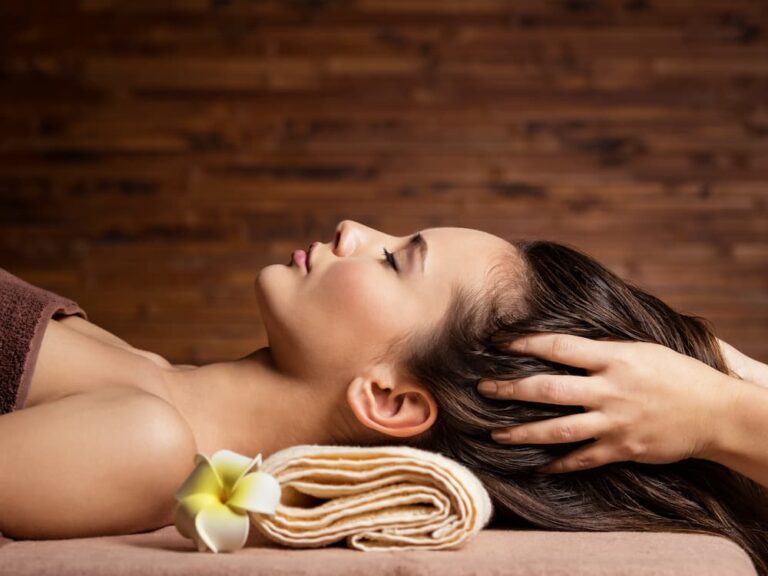 Woman with closed eyes receiving a relaxing scalp and hair massage at a spa, illustrating a perfect activity for a luxurious girls' day out focused on pampering and self-care maintenance.