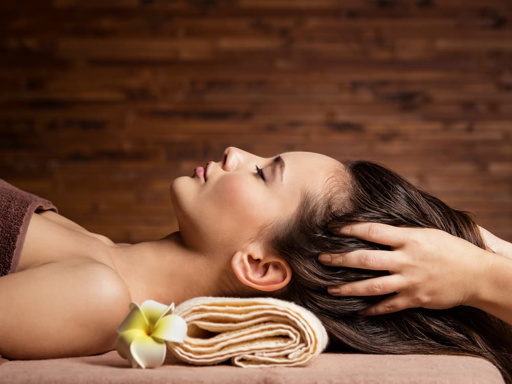 Woman with closed eyes receiving a relaxing scalp and hair massage at a spa, illustrating a perfect activity for a luxurious girls' day out focused on pampering and self-care maintenance.